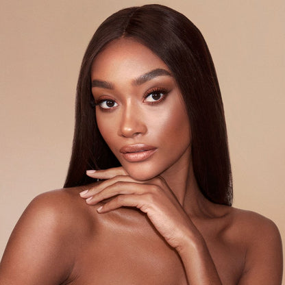 A deep-tone brunette model with glowy, face base wearing smokey brown eye makeup with bronzed, luminous face.