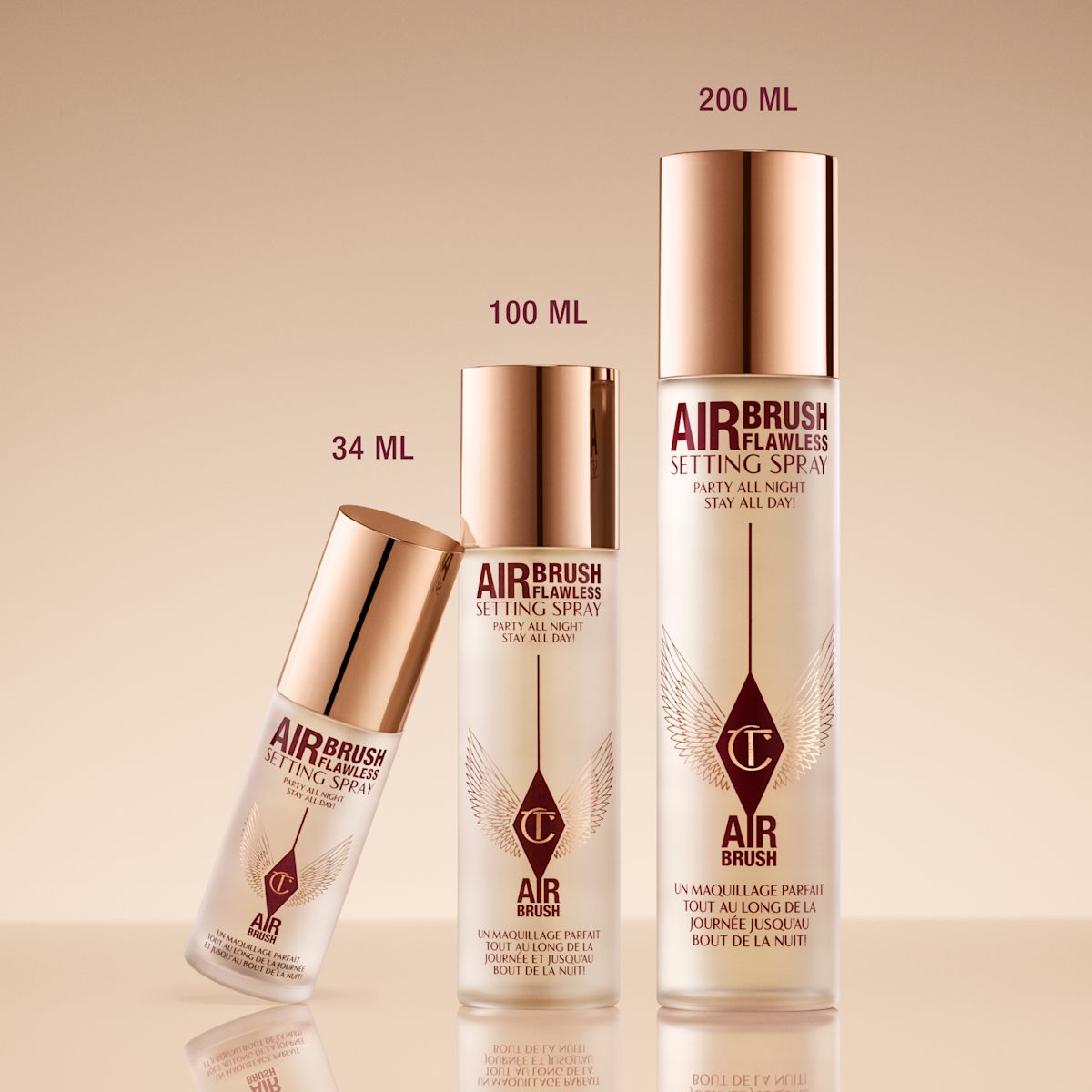 Three bottles of Airbrush Flawless Setting Spray in different sizes (34 ml, 100 ml, and 200 ml) with gold caps and a beige background.