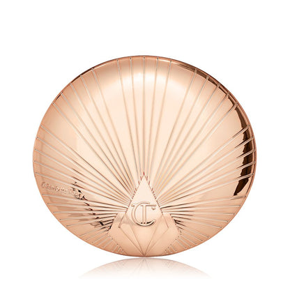 A closed, pressed powder compact in golden, metallic packaging with a starburst pattern on the lid.