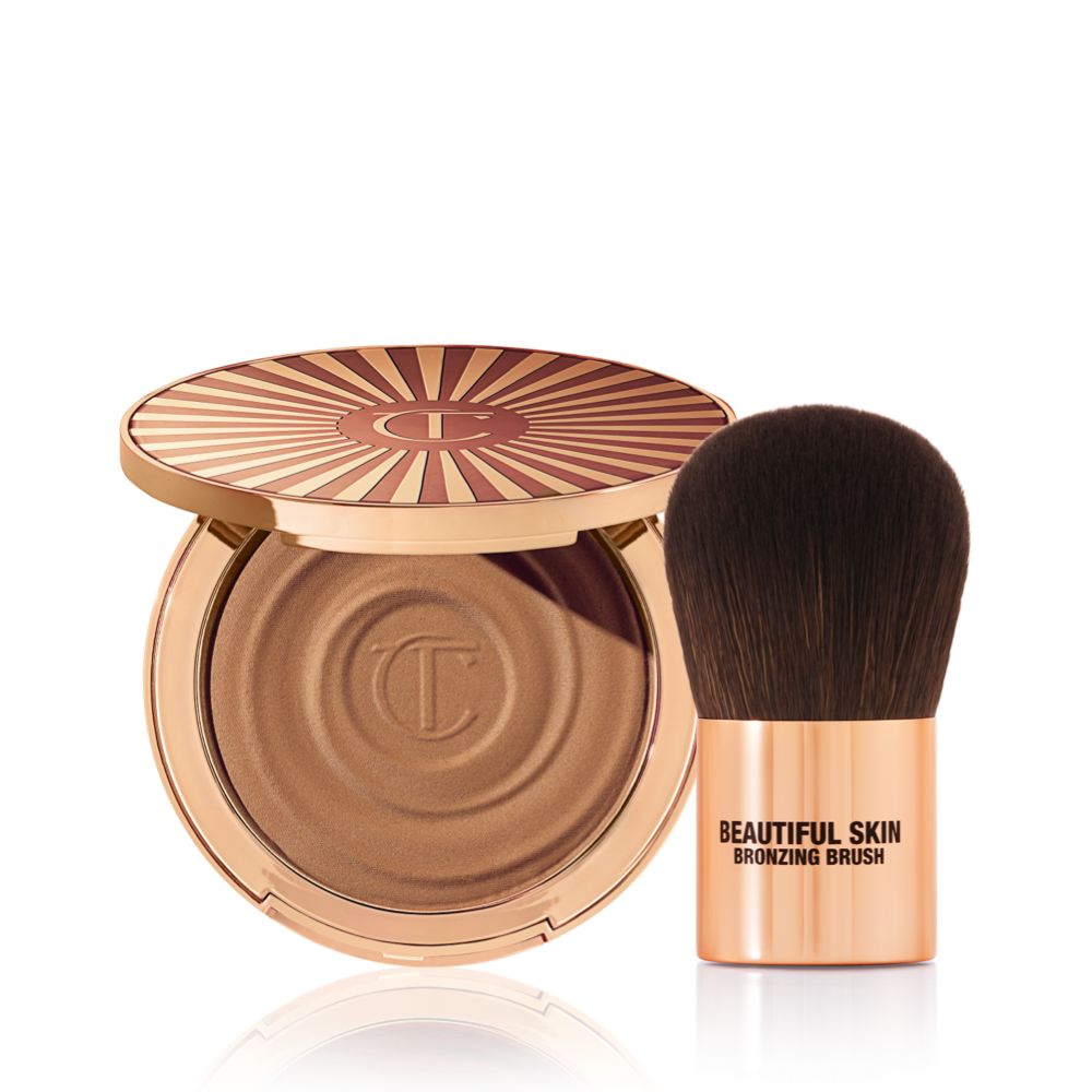 An open cream bronzer compact with gold-coloured packaging with a bronzer brush with soft,d ark-brown-coloured bristles and a golden-coloured handle.