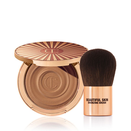 An open cream bronzer compact with gold-coloured packaging with a bronzer brush with soft,d ark-brown-coloured bristles and a golden-coloured handle.
