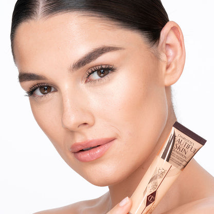 Medium-light-tone brunette model wearing glowy, skin-like foundation with a satin finish with nude lipstick and subtle eye makeup.
