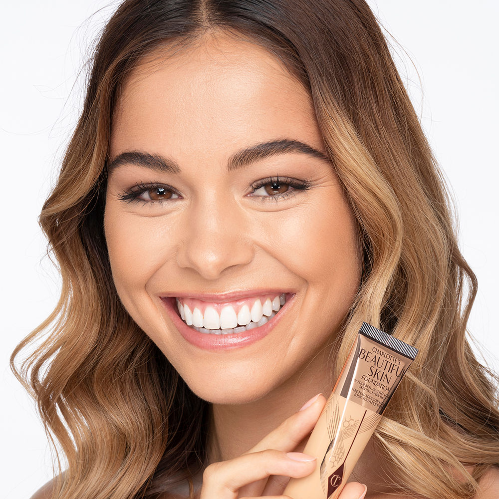 Medium-light-tone brunette model wearing glowy, skin-like foundation with a fresh, satin finish with a nude lipstick, and subtle eye makeup.