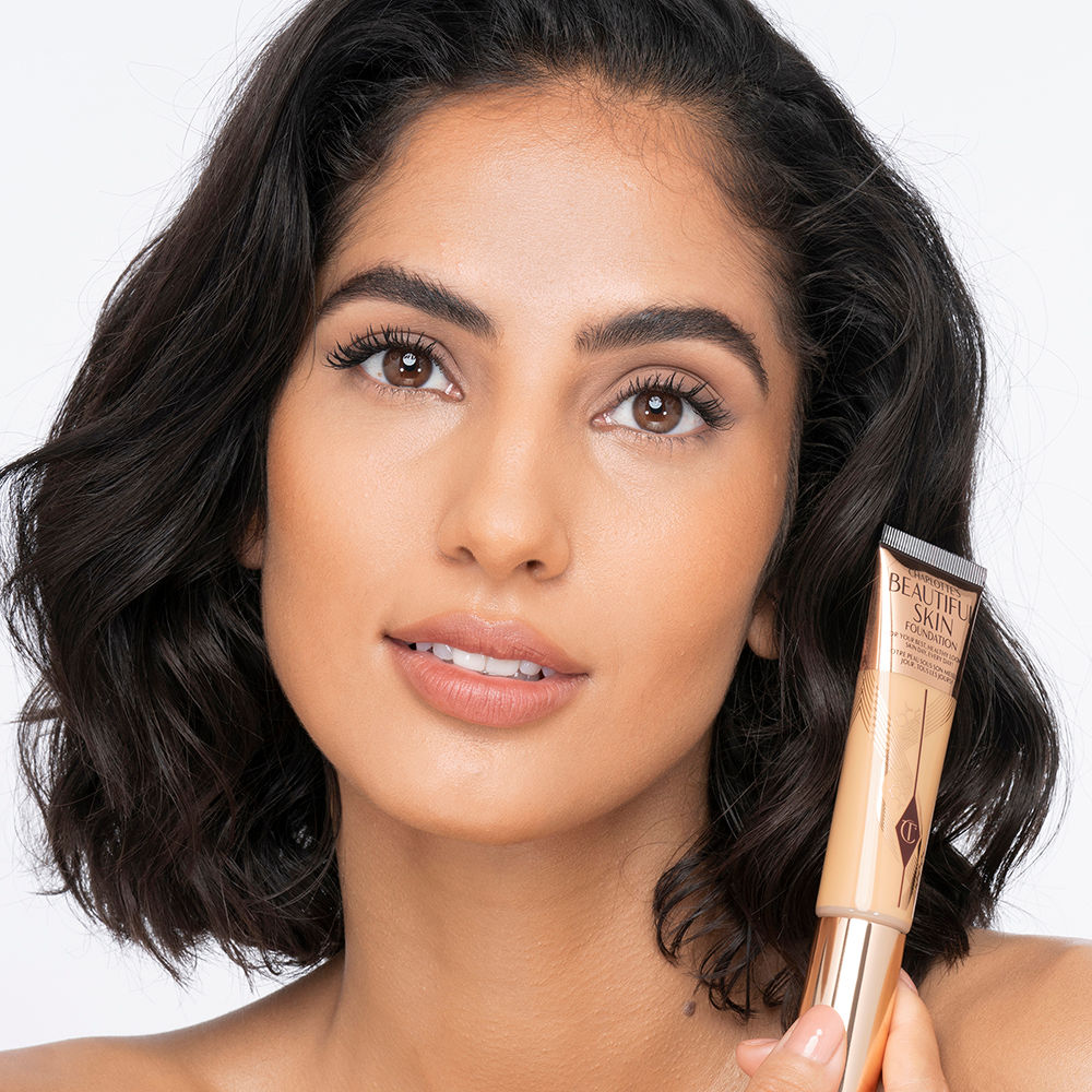 Medium-light-tone brunette model wearing glowy, skin-like foundation with a fresh, satin finish with a nude lipstick, and subtle eye makeup.