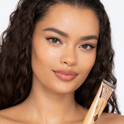 A medium-dark-tone brunette model wearing glowy, skin-like foundation that covers her blemishes and gives the appearance of clean, bouncy, and fresh skin.