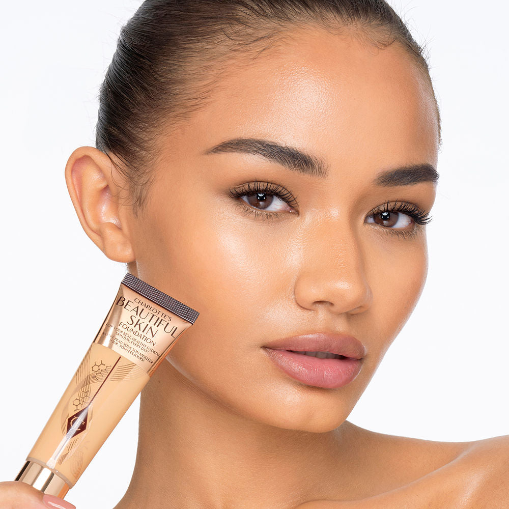 Deep-tone model with glowy, flawless skin, wearing skin-like foundation that adds a youthful glow and looks natural along with nude pink lipstick and subtle everyday eye makeup.