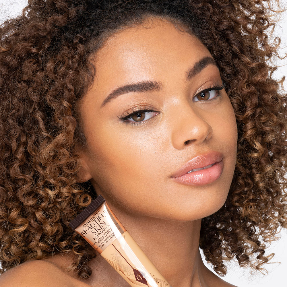 Medium-dark-tone brunette model wearing glowy, skin-like foundation with a fresh, satin finish with a nude lipstick, and subtle eye makeup.