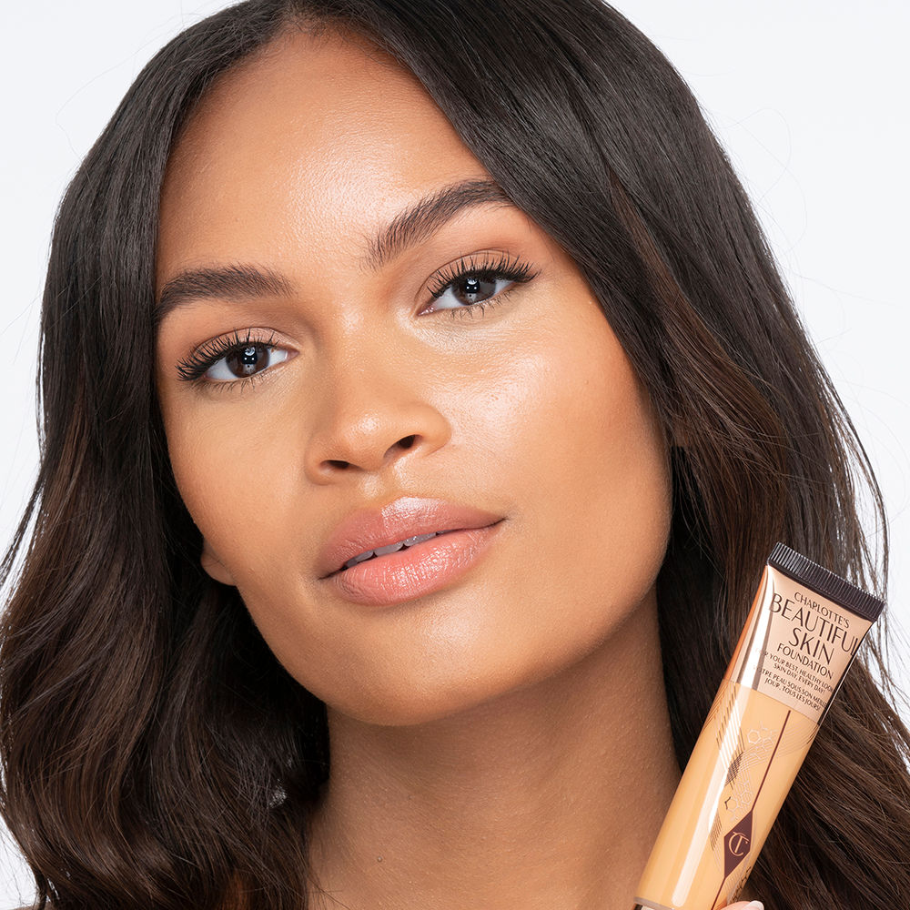 Medium-dark-tone brunette model wearing glowy, skin-like foundation with a satin finish with nude lipstick and subtle eye makeup.