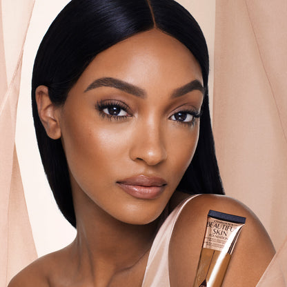 Dark-tone brunette model wearing glowy, skin-like foundation with a satin finish with nude lipstick and subtle eye makeup.