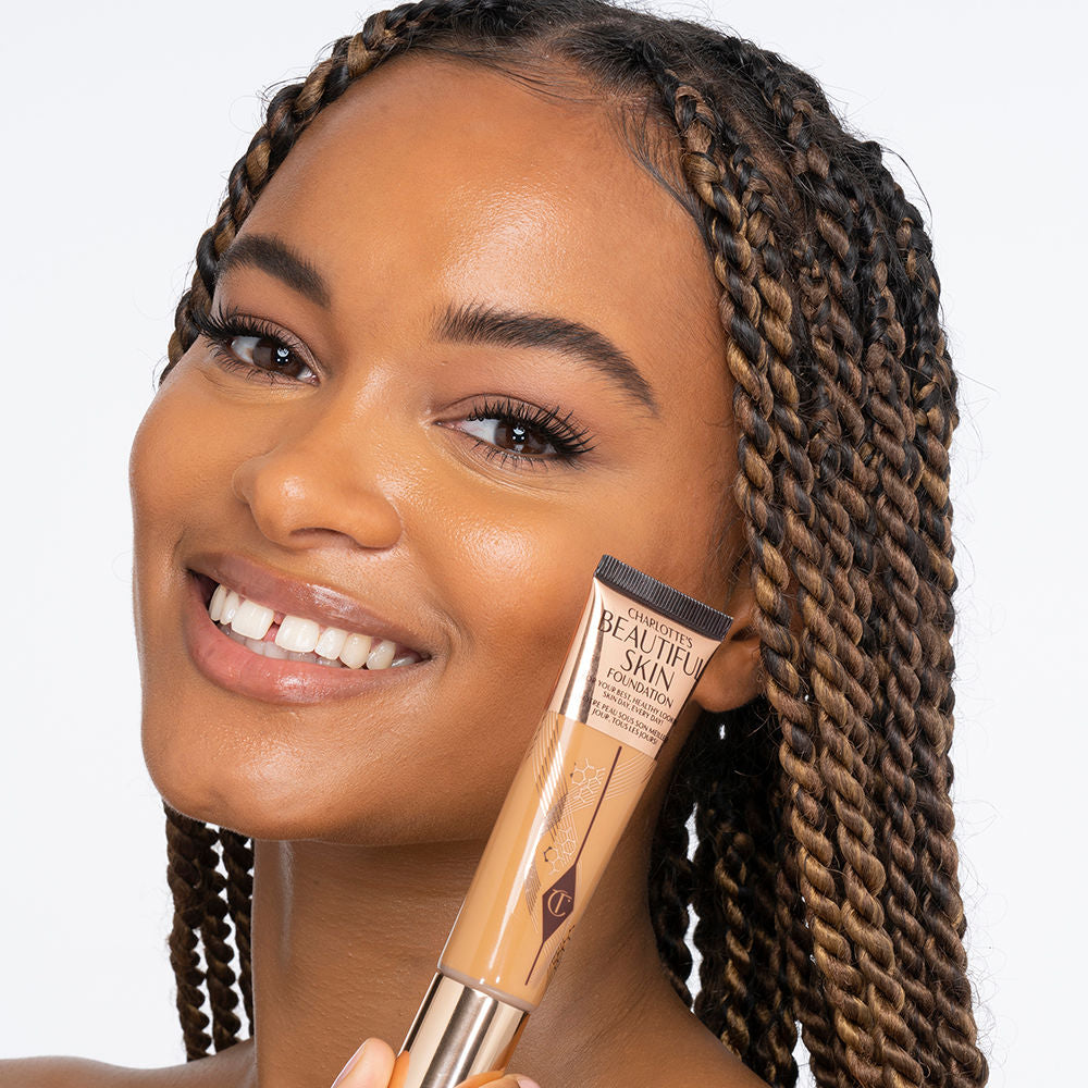 Dark-tone brunette model wearing glowy, skin-like foundation with a satin finish with nude lipstick and subtle eye makeup.