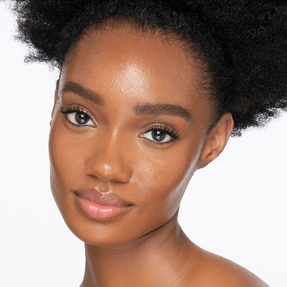 Dark-tone brunette model wearing glowy, skin-like foundation with a satin finish with nude lipstick and subtle eye makeup.