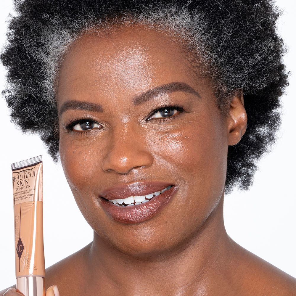 Dark-tone brunette model wearing glowy, skin-like foundation with a satin finish with nude lipstick and subtle eye makeup.