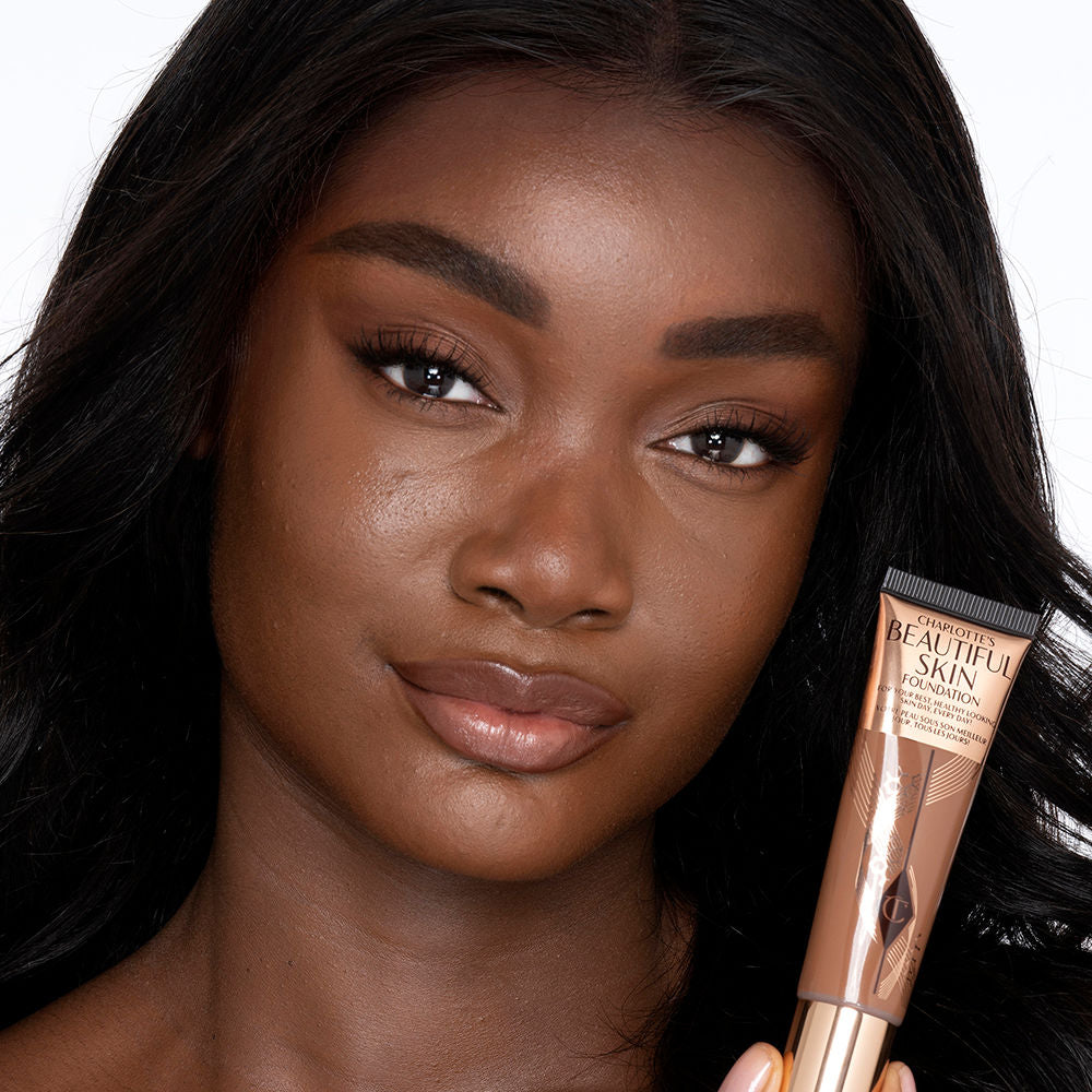 Deep-tone brunette model with brown eyes wearing nude pink lipstick with a skin-like foundation with a flawless, dewy finish.