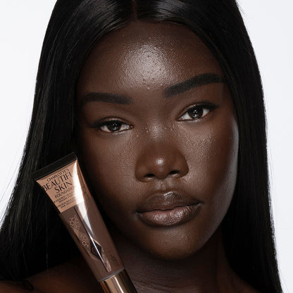 Deep-tone brunette model with brown eyes wearing nude pink lipstick with a skin-like foundation with a flawless, dewy finish.