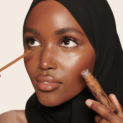 Deep-tone model with brown eyes wearing a radiant, concealer that brightens, covers blemishes, and makes her skin look fresh along with nude lip gloss and subtle eye makeup.