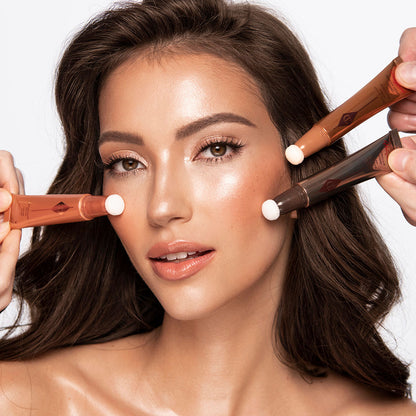 Medium-tone brunette model wearing glowy, nude coral-pink soft glam makeup look while getting blush and contour applied from liquid highlighter blush wands and a liquid contour wand.