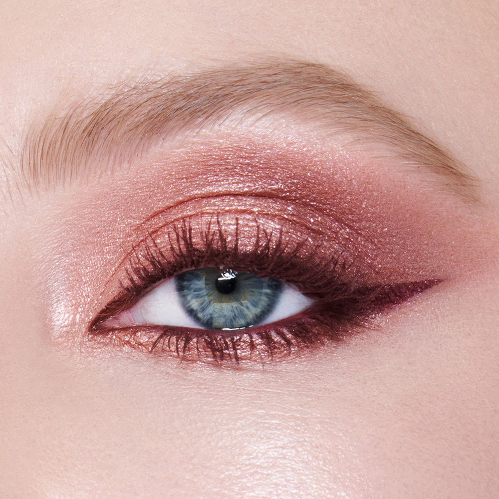 Single-eye close-up of a fair-tone model with blue eyes wearing eye makeup in shades of pearlescent rose gold, dusky rose, berry brown and rose-bud pink with berry-brown eyeliner and dark brown mascara.