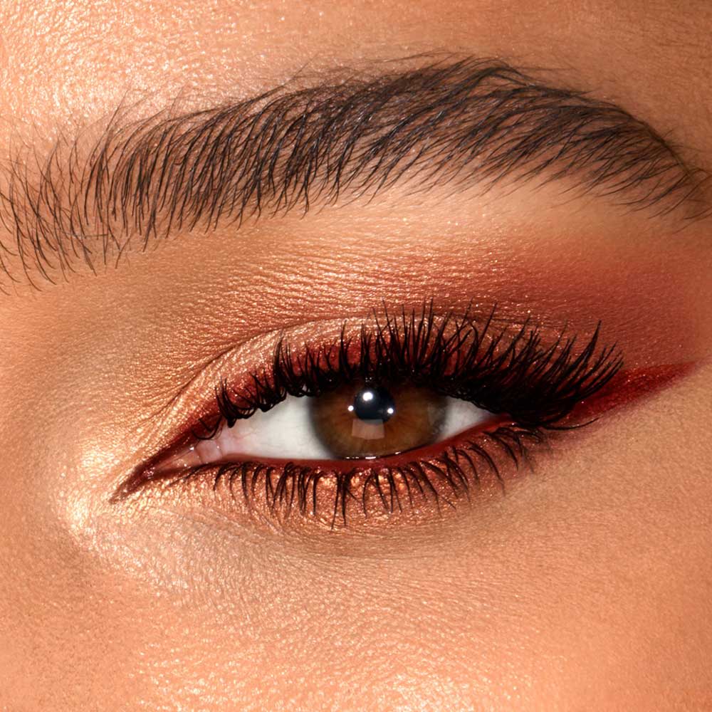 Eye close-up of a medium skin model with brown eyes wearing shimmery copper and golden eyeshadows with a brown eyeliner on the upper lid and on the lower waterline.