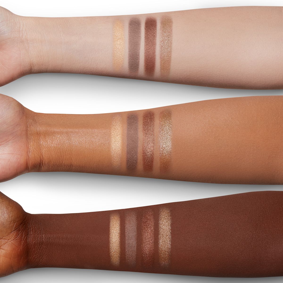 Arm swatches of four shimmery eyeshadows in champagne, bronze, and smokey grey colours on fair, tan, and deep skin.