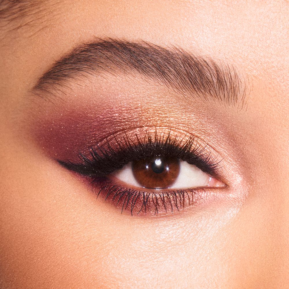 Eye close-up of a light-tone model with brown eyes wearing a shimmery plum and gold eye look.