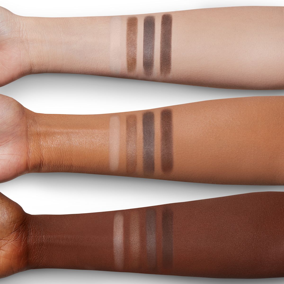 Arm swatches of four matte eyeshadows in cream, tan, taupe, and chocolate colours on fair, tan, and deep skin.