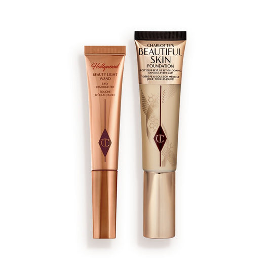 Highlighter wand in light gold-coloured packaging with a foundation wand in gold packaging with a ashy brown-beige-coloured body to show the shade of the foundation inside, and a gold-coloured lid.
