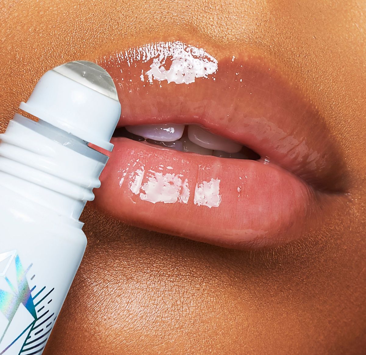 Close-up of a deep-tone model applying a nourishing, clear lip oil with a crystal roller ball applicator.