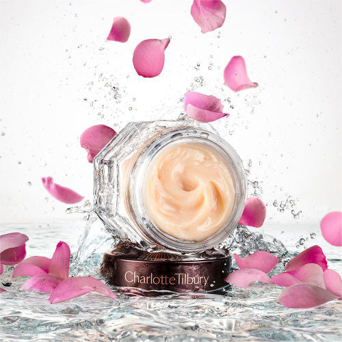 Banner with an open glass jar with thick, peach-coloured night cream and its dark-brown and gold-coloured lid placed on top of crystal-clear water with rose petals falling down on it.