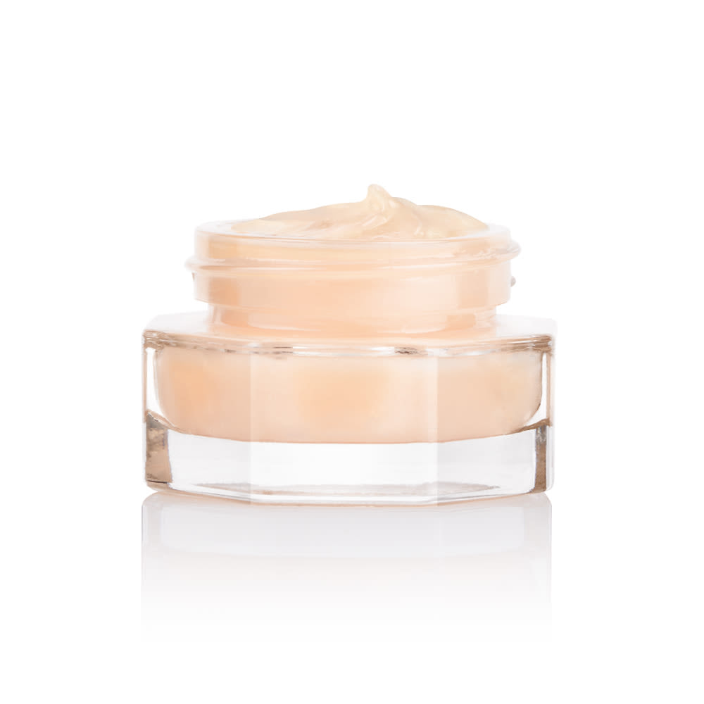 A closed, travel-sized thick and luscious dark champagne-coloured face cream in an open glass jar with a black and gold coloured lid next to it.