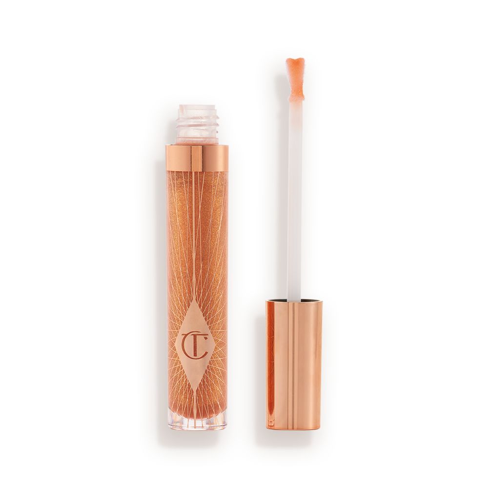 A lip gloss in a sheer gold shade in a glass tube with its heart-shaped applicator next to it.