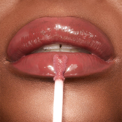 A deep-tone model applying a berry-pink lip gloss on her lips with a heart-shaped applicator.