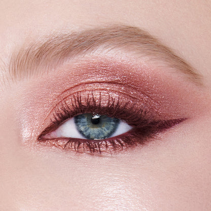 Single-eye close-up of a fair-tone model with blue eyes wearing eye makeup in shades of pearlescent rose gold, dusky rose, berry brown and rose-bud pink with berry-brown eyeliner and dark brown mascara.