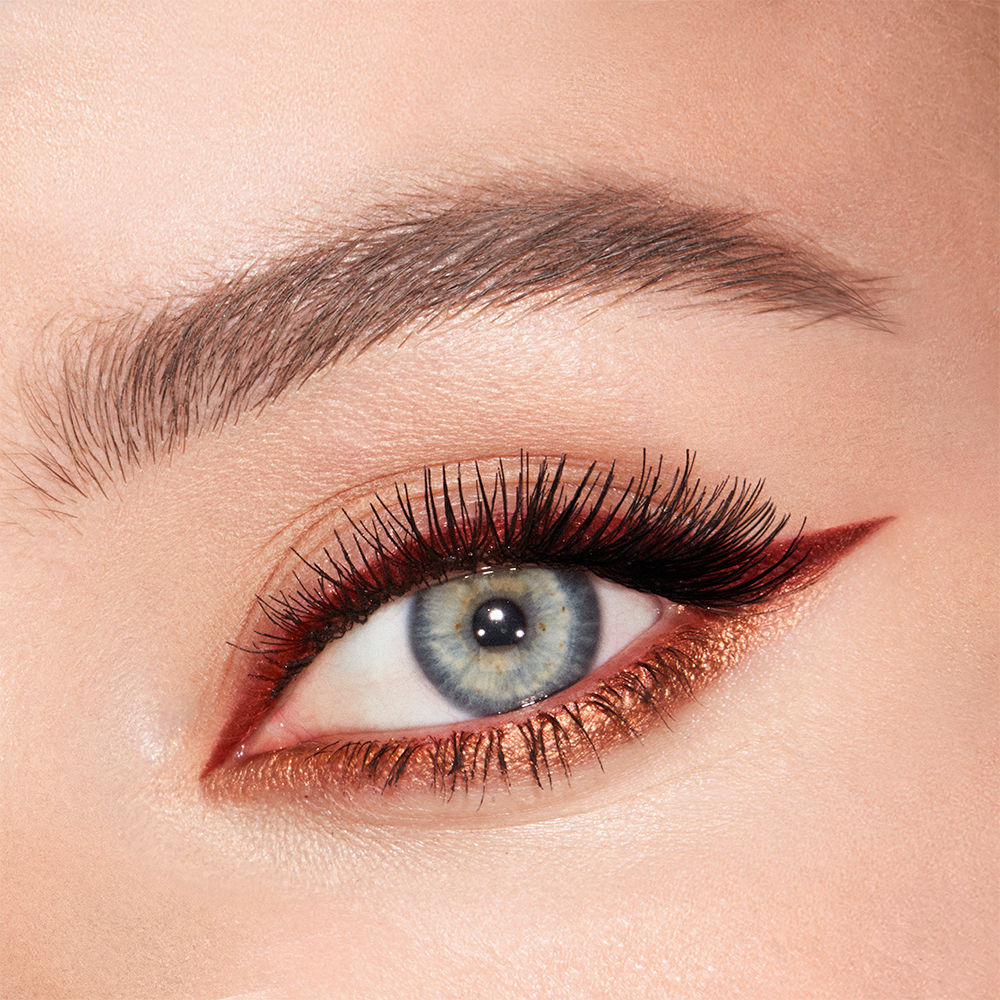 Eye close-up of a fair-tone, blue-eyed model wearing a matte, rust-coloured eyeliner on the upper lid and shimmery copper-coloured liner on the lower waterline.