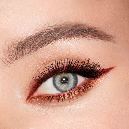 Eye close-up of a fair-tone, blue-eyed model wearing a matte, rust-coloured eyeliner on the upper lid and shimmery copper-coloured liner on the lower waterline.