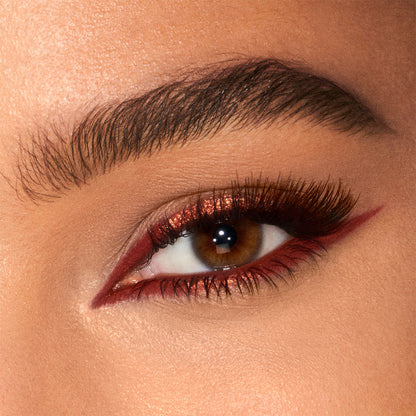Eye close-up of a tanned model wearing a glistening, coppery-rust-coloured eyeliner on the upper lid and lower waterline.