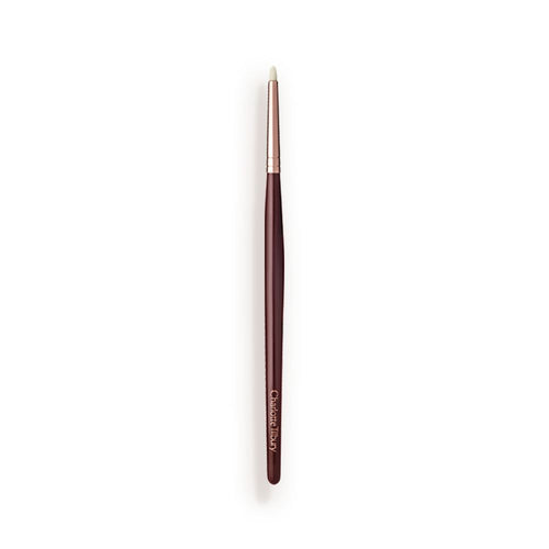 A slim eyeshadow brush with white-coloured bristles with a rose-gold and dark crimson handle.