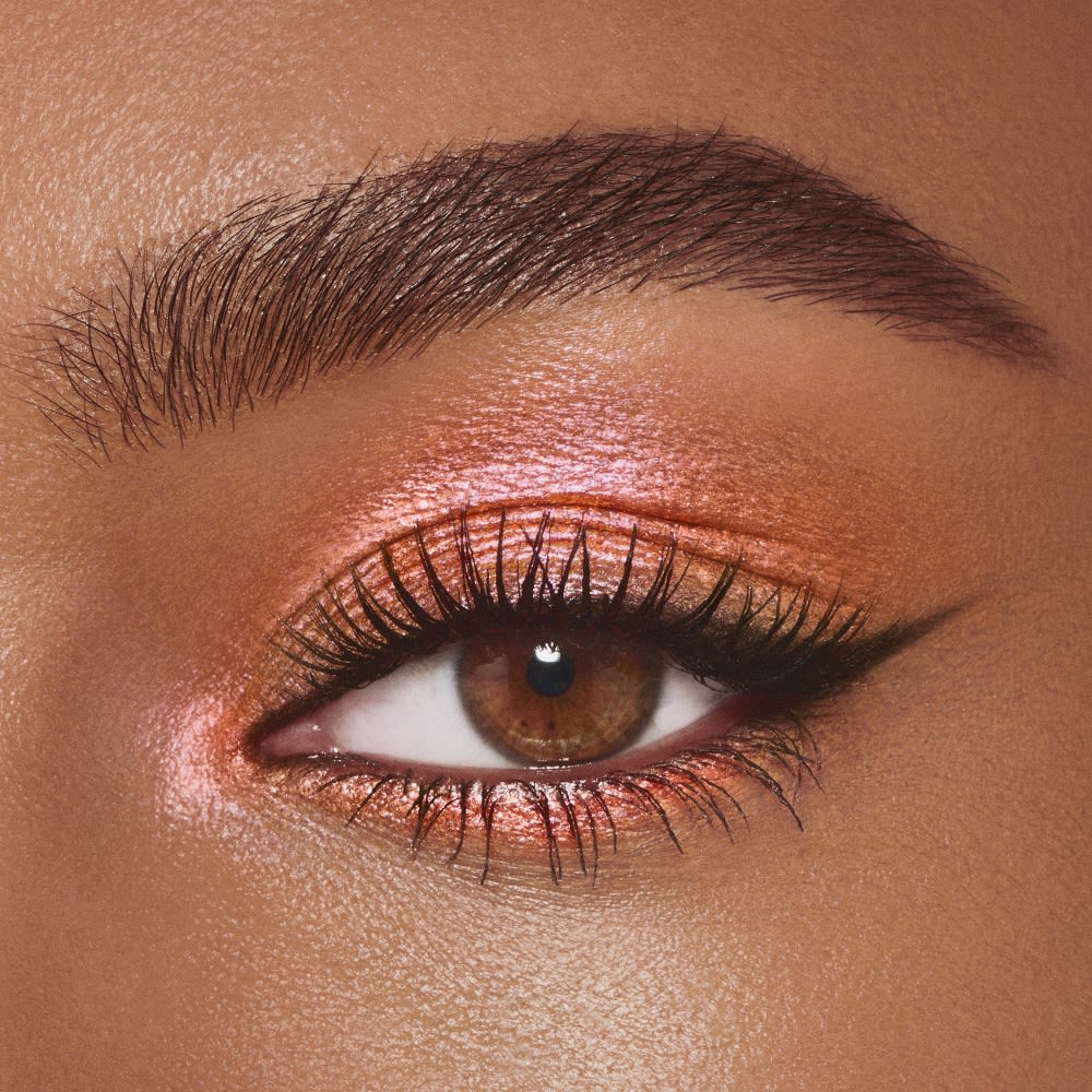 Single-eye close-up of a deep-tone model with brown eyes wearing golden pink duo-chrome-effect cream eyeshadow with a duo-chrome metallic finish,