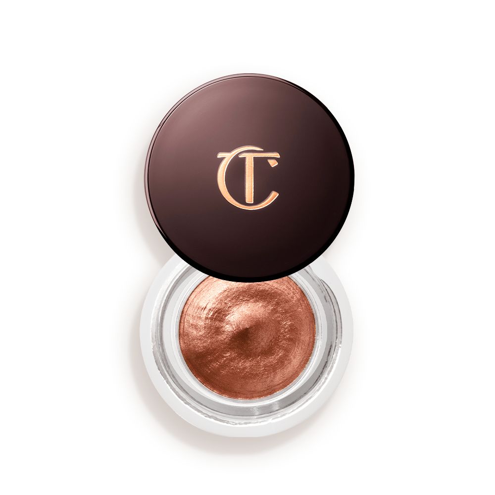 An open glass pot with shimmery russet rose cream eyeshadow with golden-peach sparkle and its lid placed next to it.