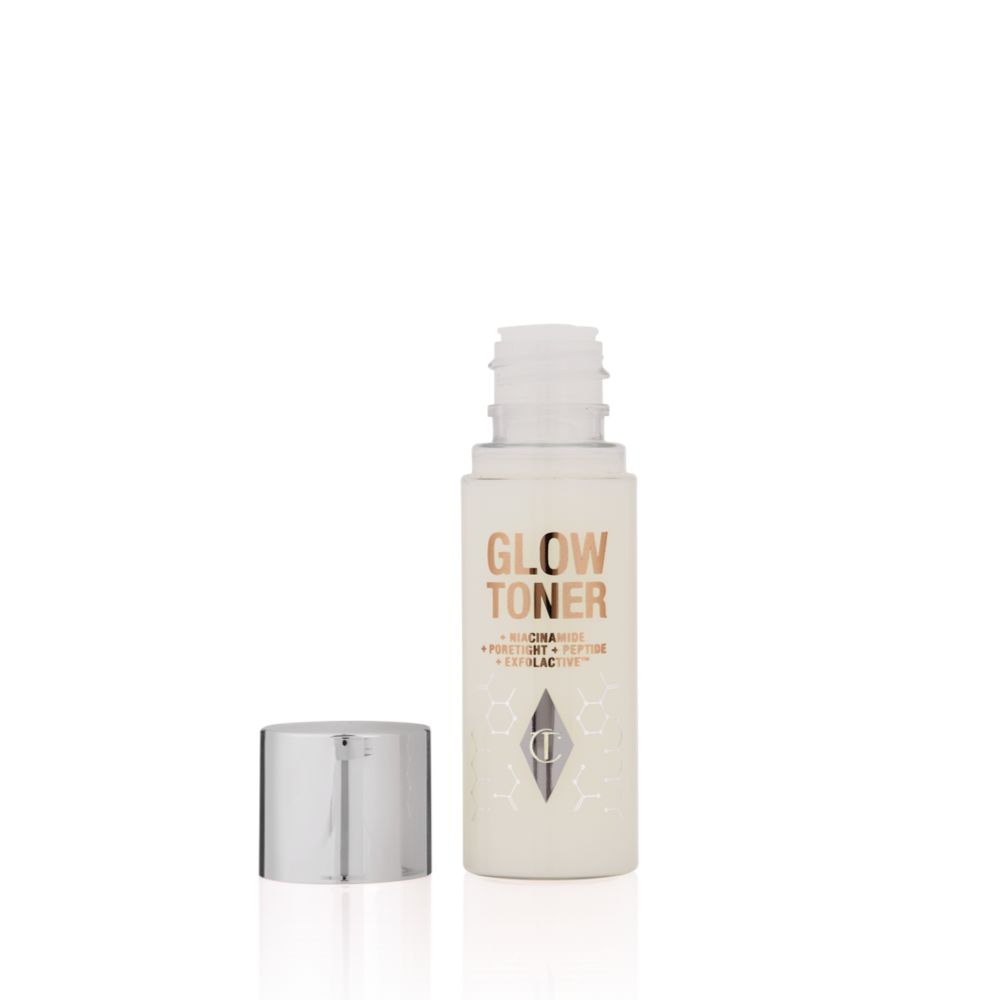 An open, travel-size, clear bottle filled with luminous, cream-coloured watery toner with its silver-coloured lid next to it.