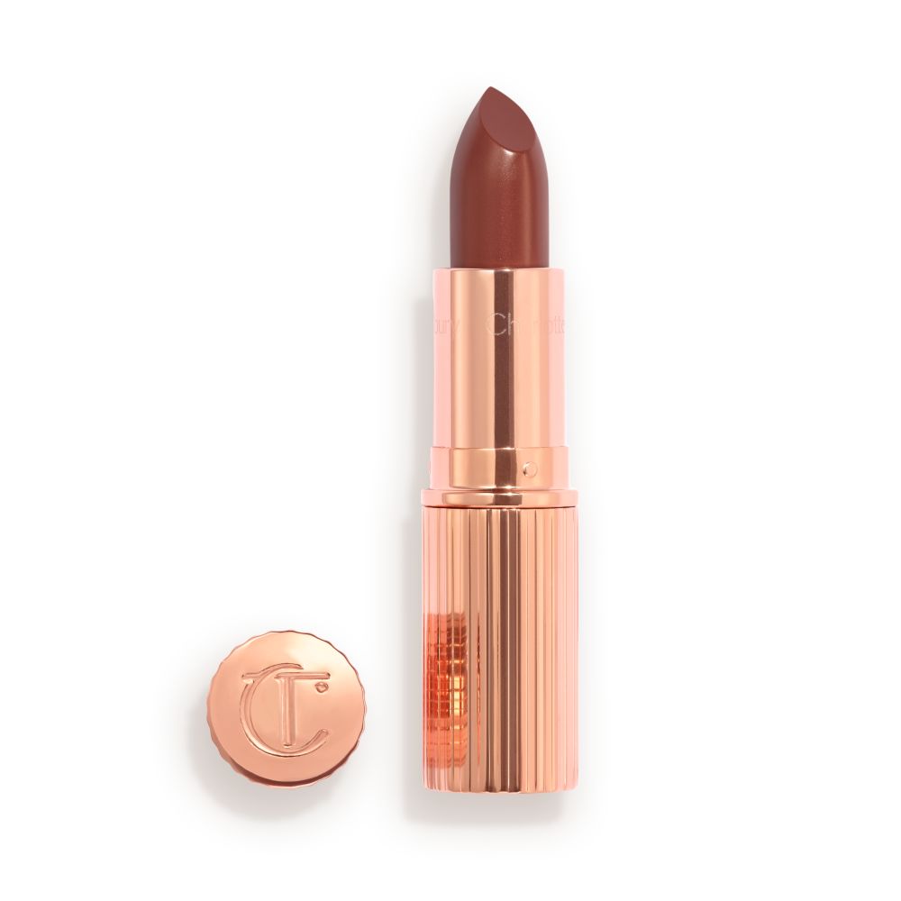 Opened, berry-pink lipstick in a metallic, golden case with its lid that's embossed with CT placed next to it.