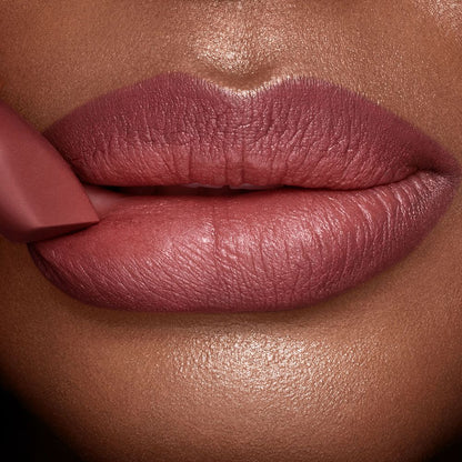 A deep tone model with glowing skin wearing a berry-pink lipstick with the lipstick gently pressed to the lower lip.