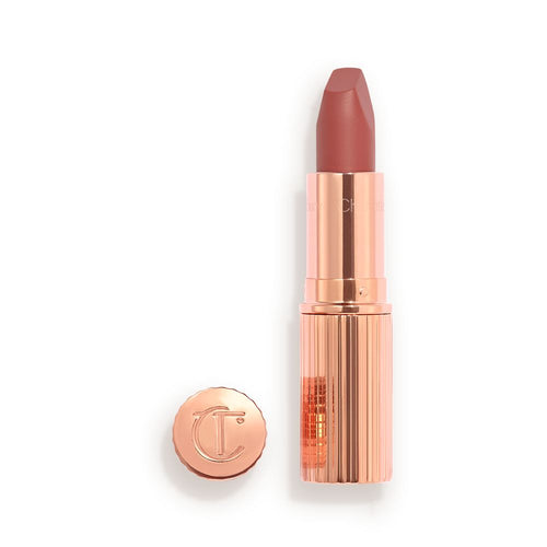 Opened, berry-pink lipstick in a metallic, golden case with its lid that's embossed with CT placed next to it.