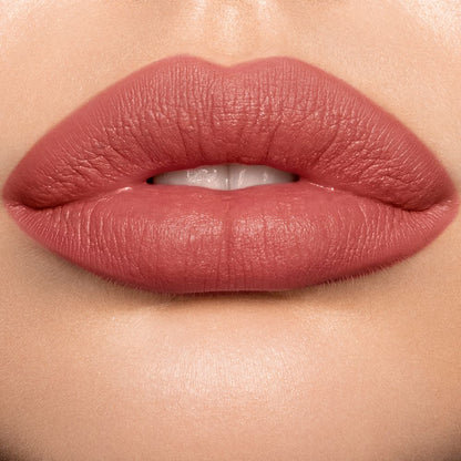 Lips close-up of a light skin model wearing a pigmented, matte lipstick in a golden peachy-pink colour.