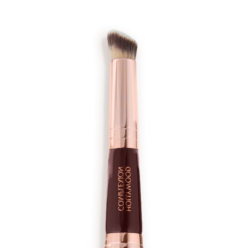 Close-up of a concealer brush with fawn and dark brown bristles with a rose-gold and dark crimson handle.