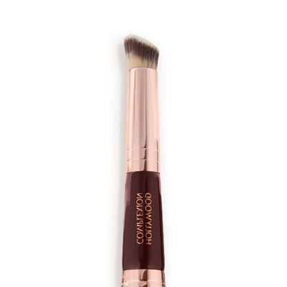 Close-up of a concealer brush with fawn and dark brown bristles with a rose-gold and dark crimson handle.