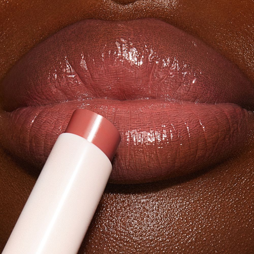 Lips close-up of a deep-tone model wearing a peachy nude rose lipstick lip balm.