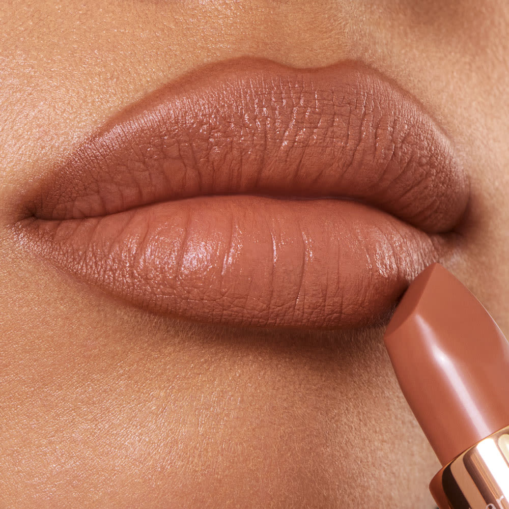 Lips close-up of a medium-tone model wearing a fresh, neutral nude peach lipstick with a matte finish.