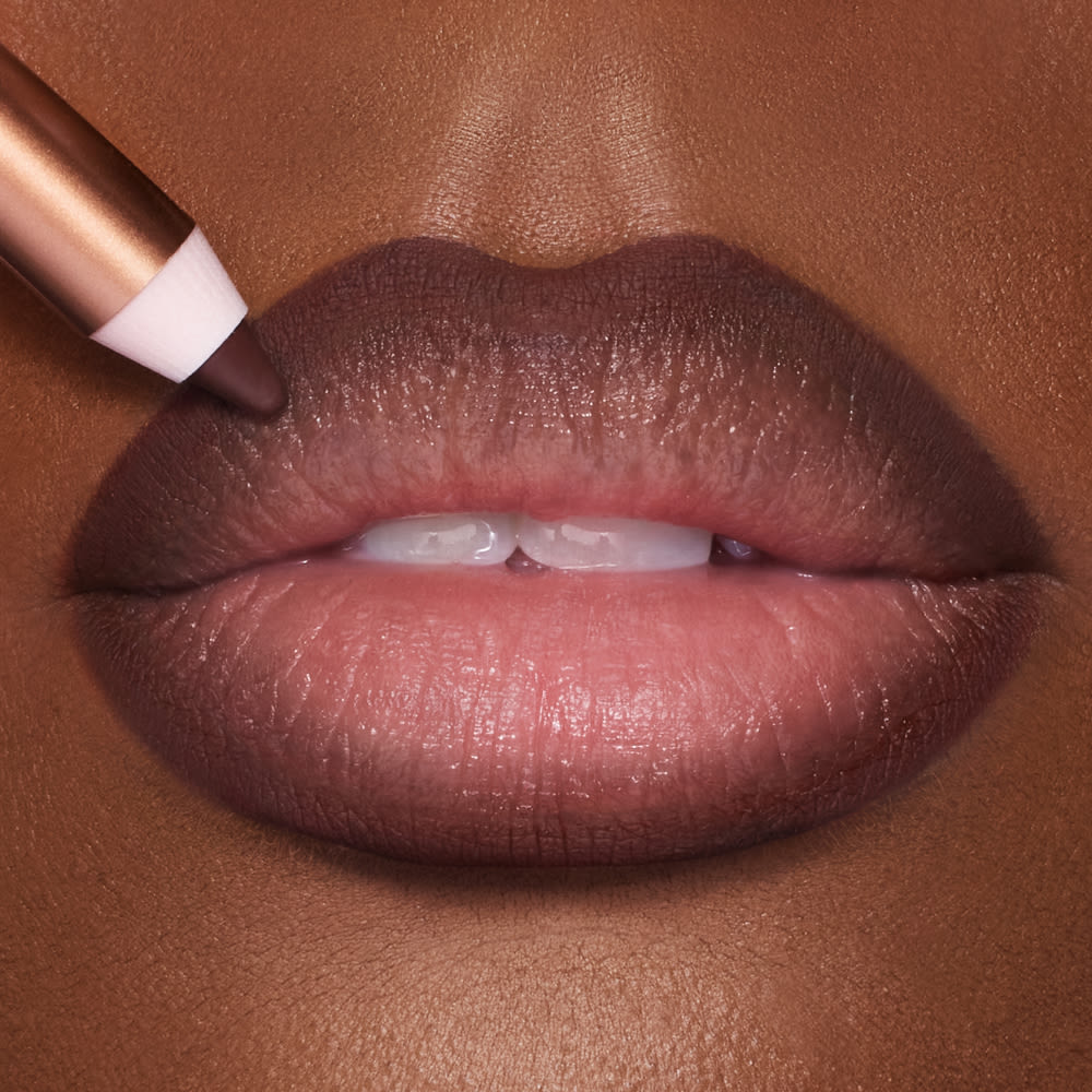 Close-up of a tanned model's lips that have a tawny-brown matte lip shade applied to them.