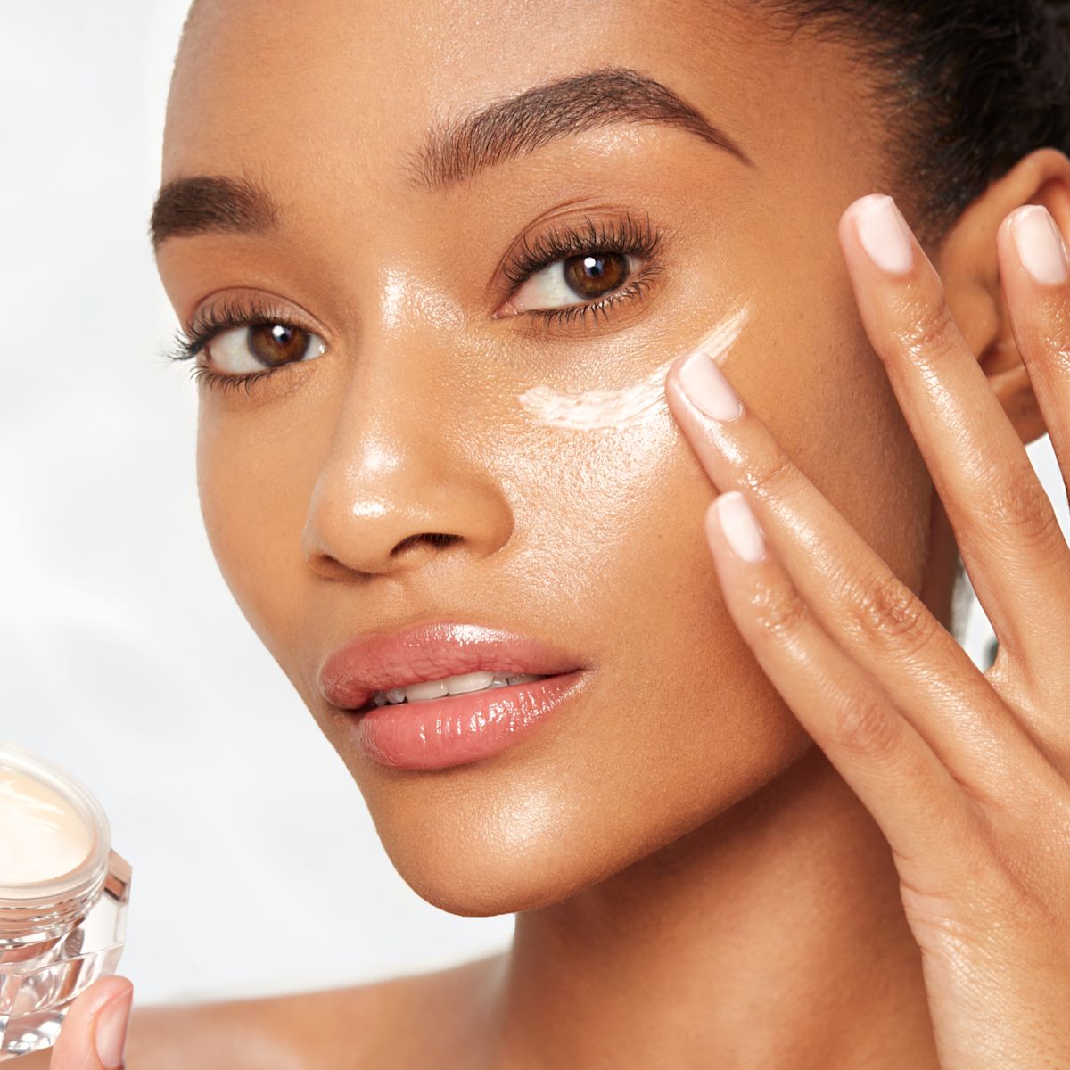 Deep-tone model with dewy, glass skin applying silky and moisturising eye cream on her under eye area.