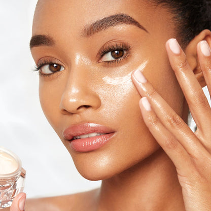 Deep-tone model with dewy, glass skin applying silky and moisturising eye cream on her under eye area.